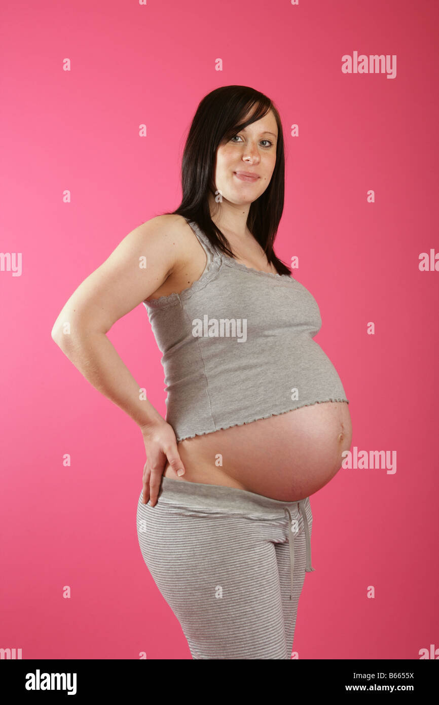 Drei Viertel Profil Aufnahme einer dunklen Haaren 38 Woche (neun Monate) schwangere Frau stehend mit den Händen auf den Hüften. Stockfoto