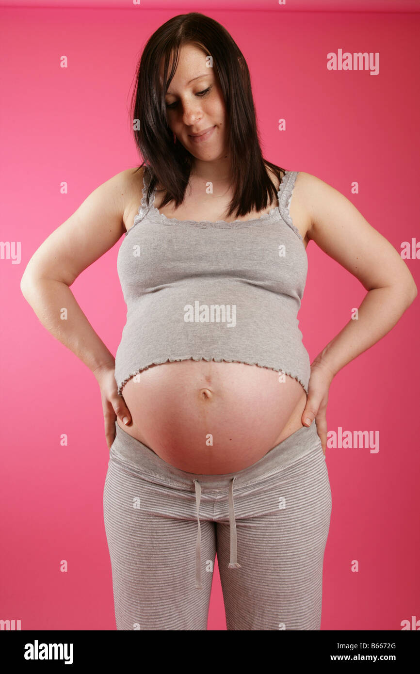 Ein Kopf auf Blick auf einen dunklen Haaren 38 Woche (neun Monate) schwangere Frau stehend tragen legere Kleidung grau. Stockfoto