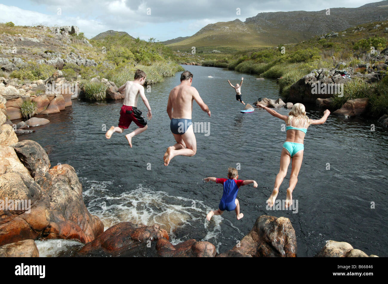 Familie und Freunde springen von den Felsen ins Meer Stockfoto