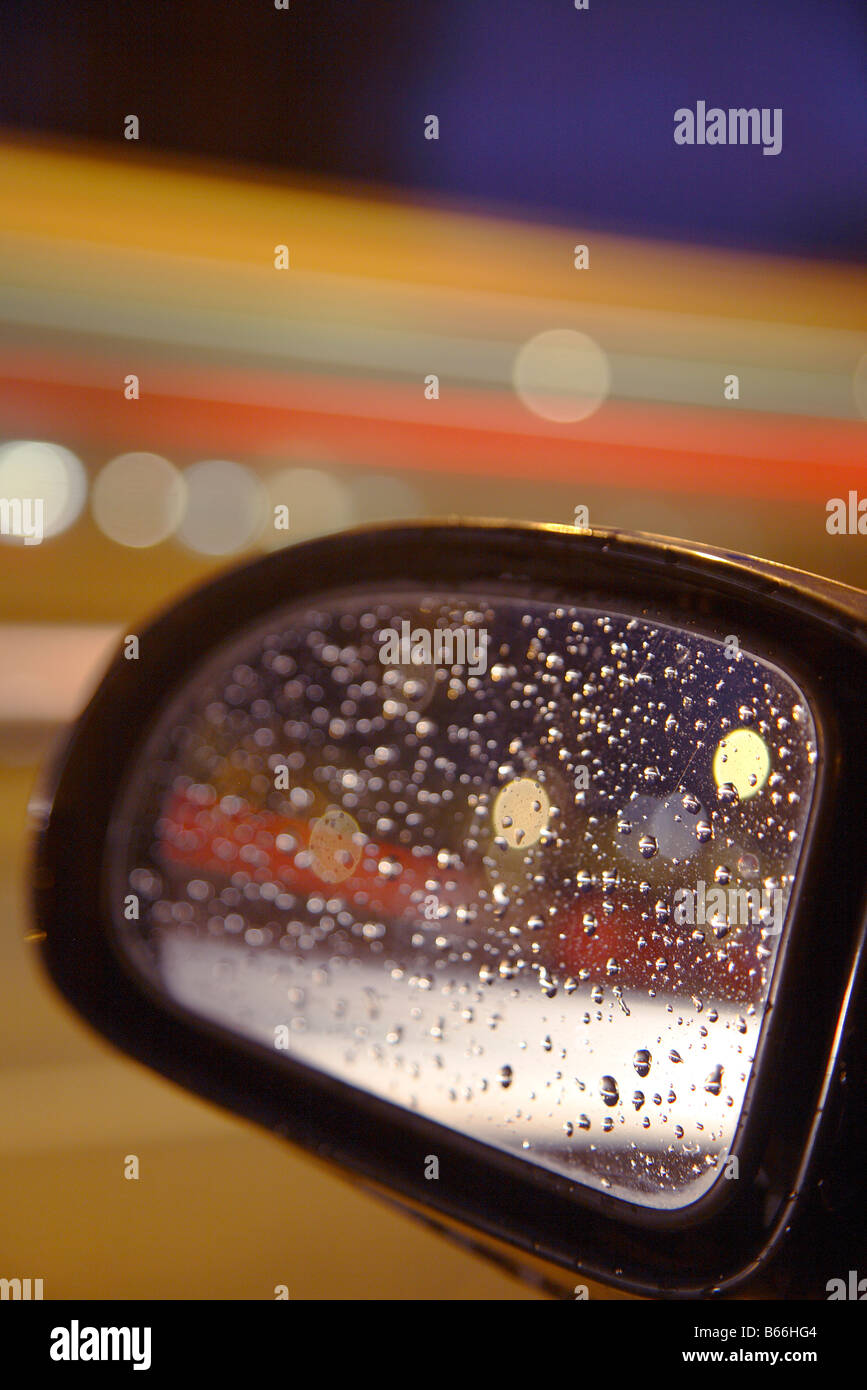Auto Rückfahrkamera Seite Spiegel Stadtbeleuchtung und Regentropfen Stockfoto