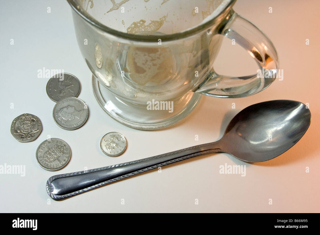 Leere Cappuccino-Glas, einem Metalllöffel auf einer weißen Fläche mit U.K Münzen; 2 10 Pence, 1 zwanzig Pence, 1 fünf Pence, 1 Schilling Stockfoto