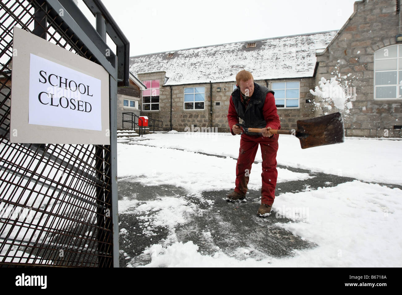 Arbeiter mit Schaufel löscht Wege außerhalb einer Schule, die in Aberdeenshire, Schottland im Winter wegen Schnee geschlossen ist Stockfoto