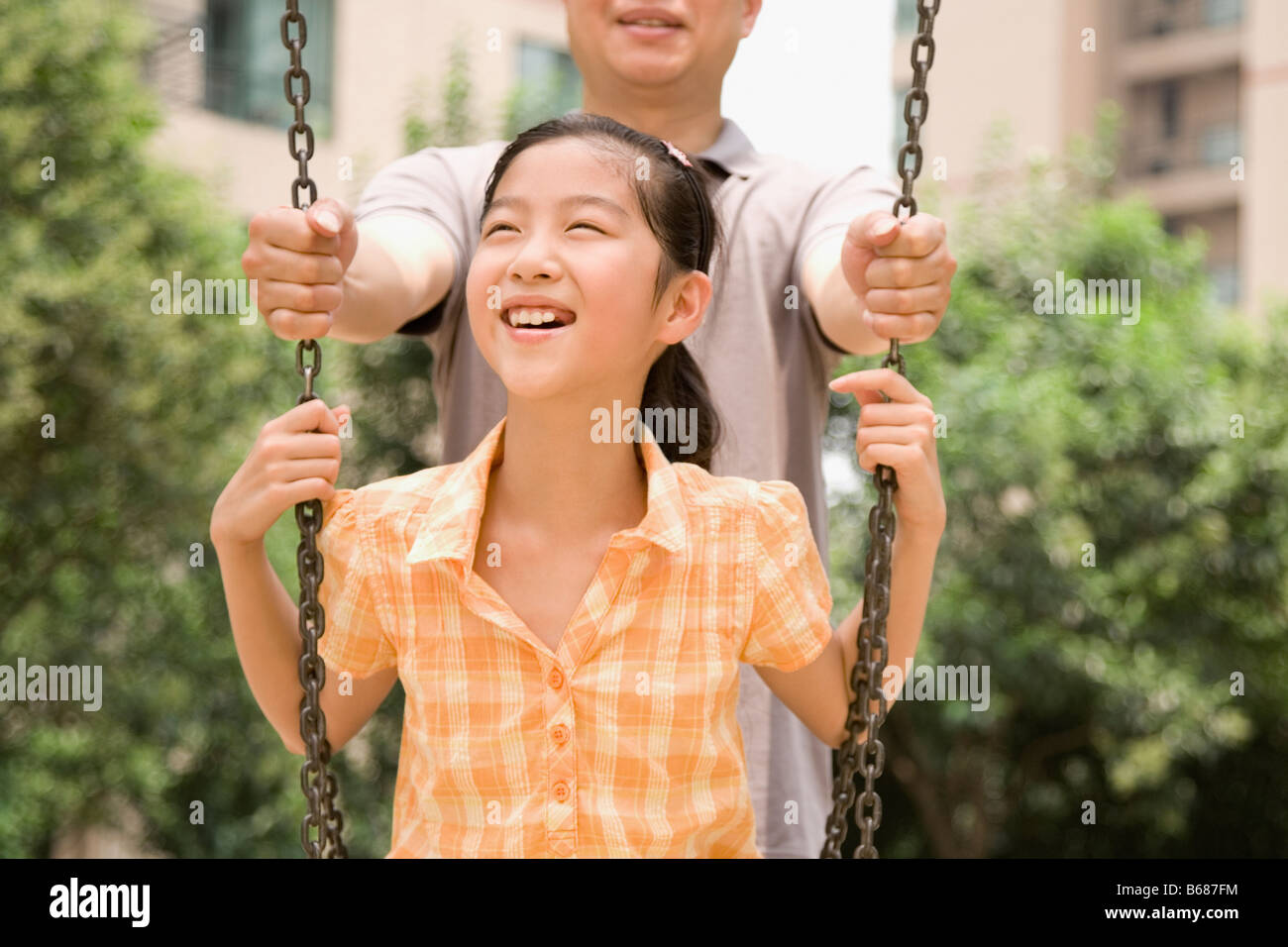 Mädchen auf einer Schaukel mit ihrem Vater hinter ihr stand lächelnd Stockfoto