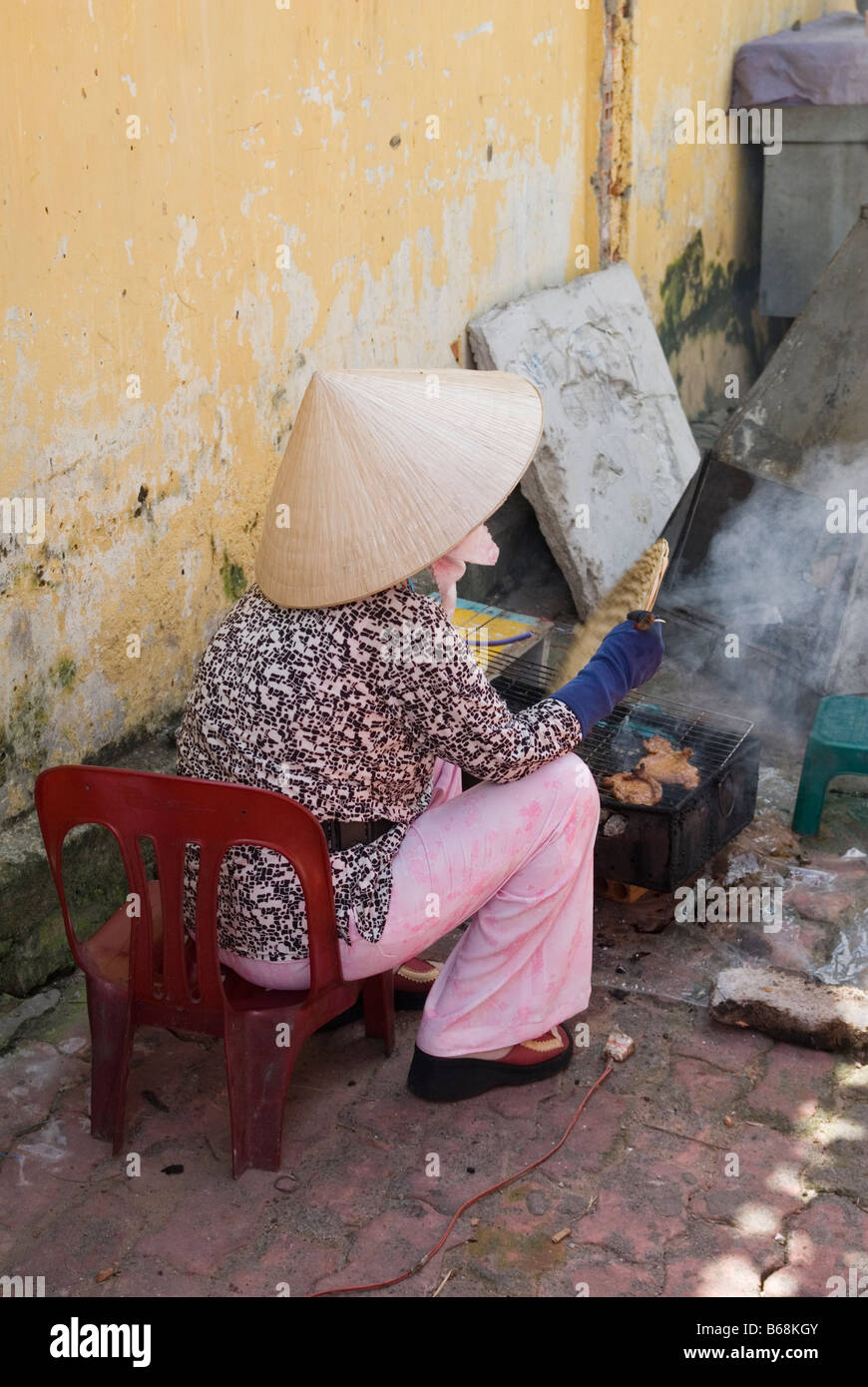 Eine street Hersteller herkömmlicher Reis hat Fans tragen ein kleines Holzkohle Grill kochen Fleisch in Ho Chi Minh City, Vietnam Stockfoto