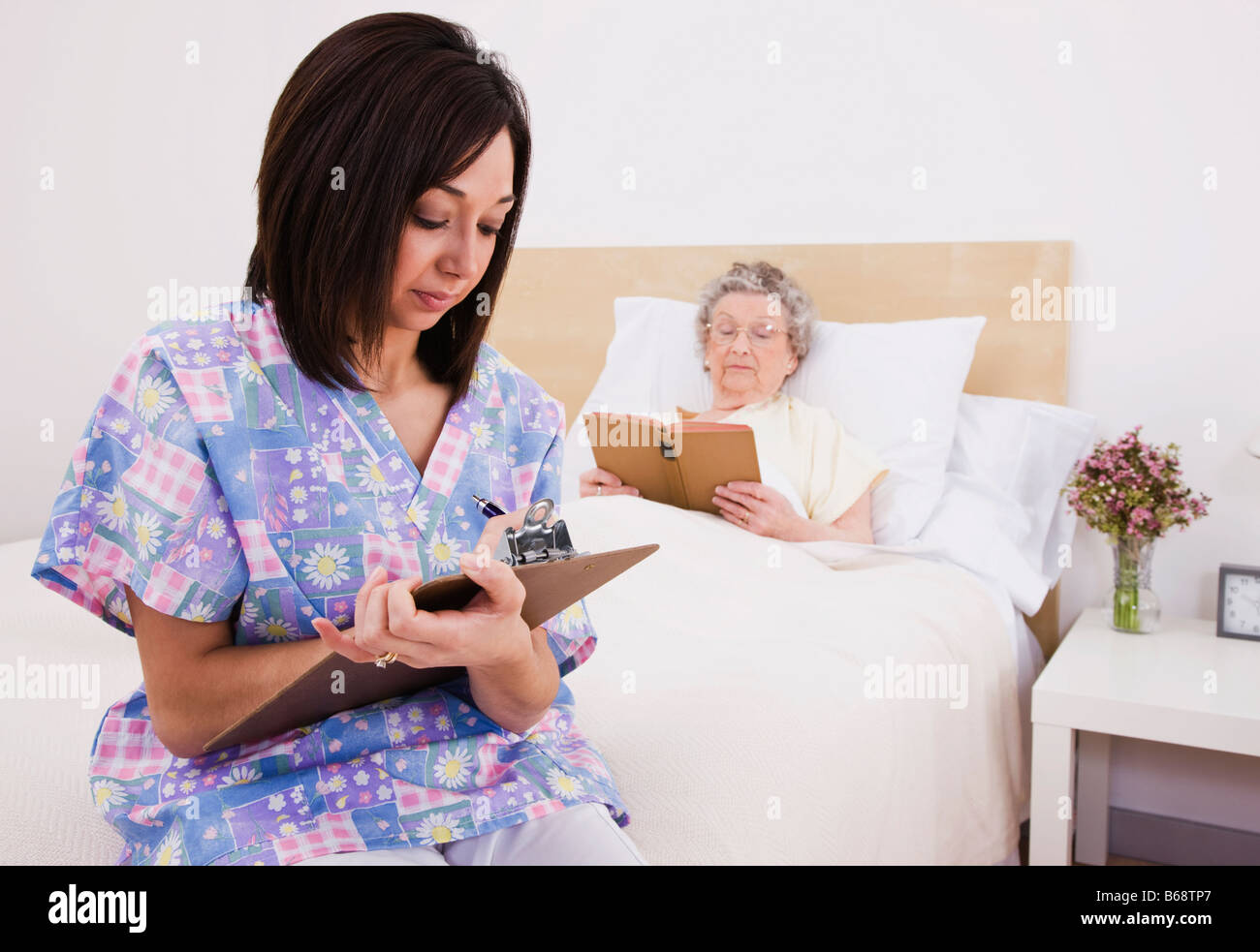 Krankenschwester, die schriftlich in der Patientenakte, senior Frau im Bett liegend in Hintergrund Stockfoto