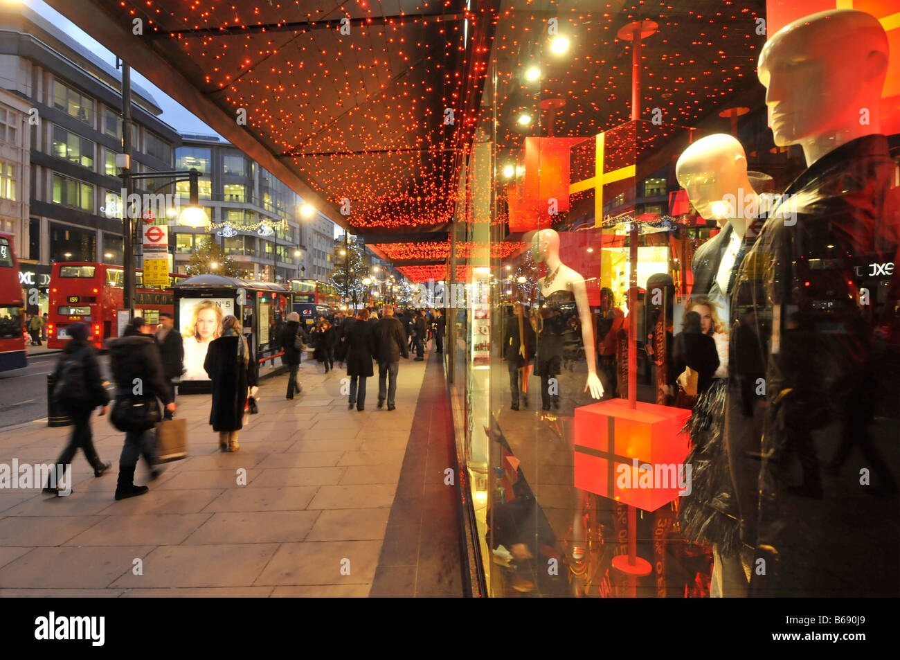 Käufer von befestigten Straßen außerhalb Department Store Fenster vorne mit Weihnachtsgeschenke auf der Oxford Street mit Weihnachtsbeleuchtung in London West End UK Stockfoto