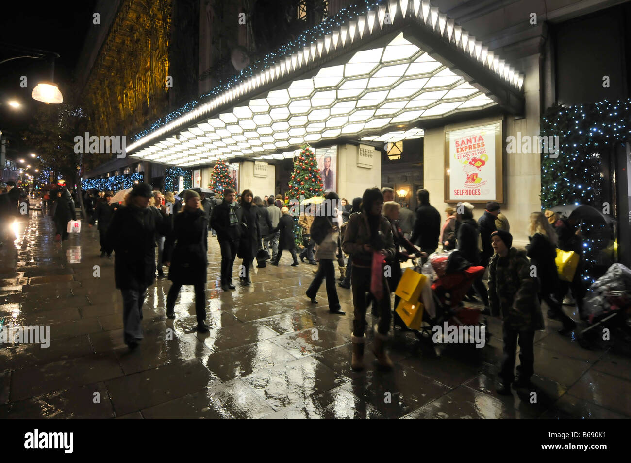 Nacht Blick geschäftigen Oxford Street Shopper & Touristen Silhouette & Weihnachten Einkaufen im Regen außerhalb Selfridges Kaufhaus Eingang London UK Stockfoto