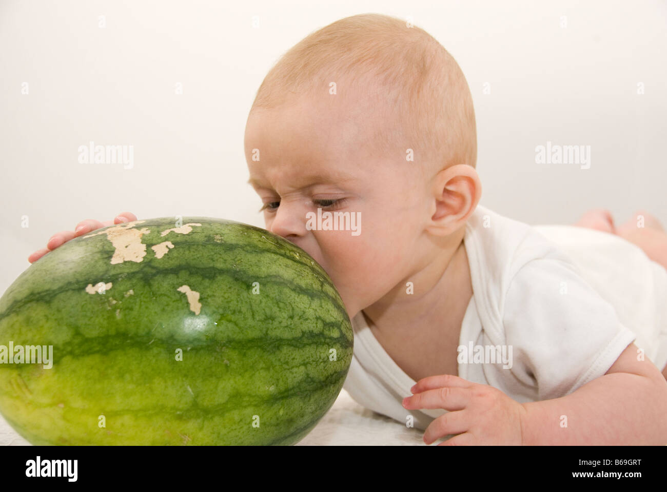 Baby Boy liegend auf Bauch versucht, eine riesige grüne Wassermelone essen ausgeschnitten auf weiß Stockfoto