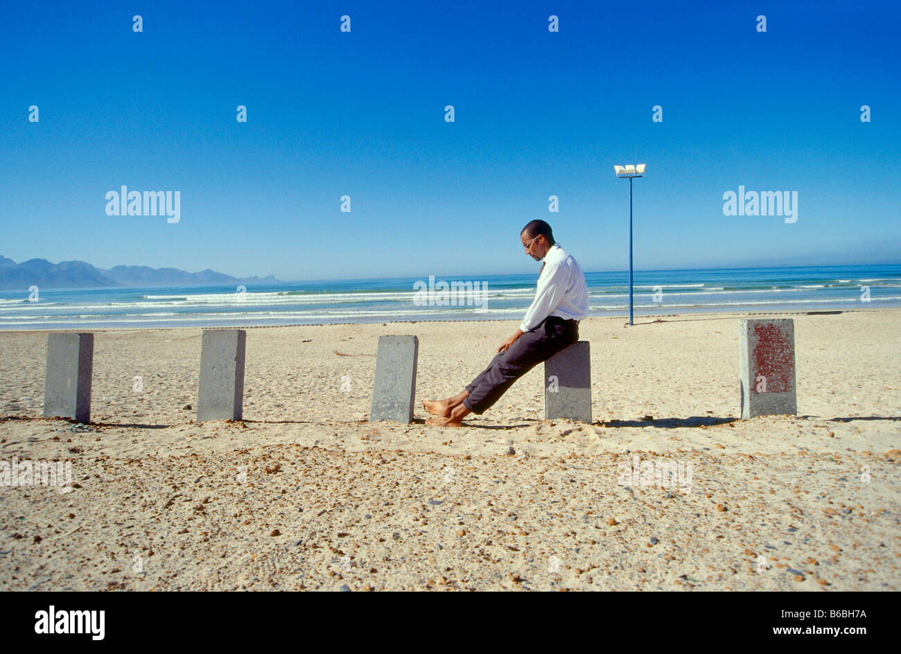 Seitenansicht der Geschäftsmann auf konkrete Pol am Strand sitzen Stockfoto