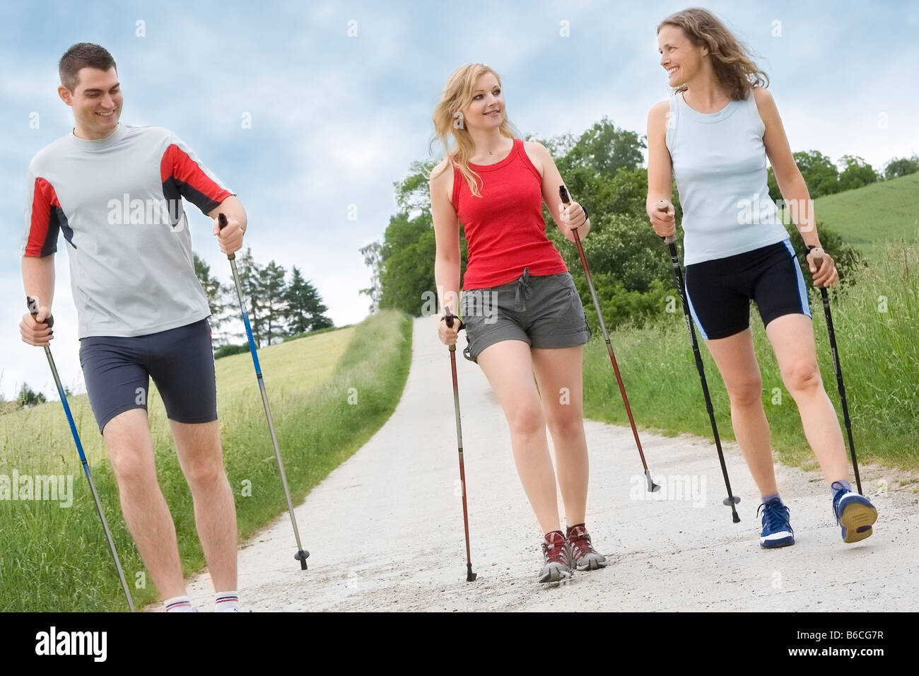 Zwei Frauen und ein Mann zu Fuß mit Wanderstöcken auf Feldweg Stockfoto