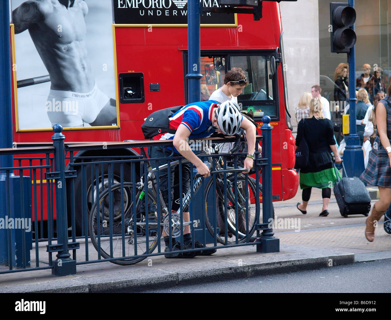Radfahrer, die Verkettung sein Fahrrad an einen Zaun mit einer riesigen Schloss Oxford Circus in London Stadt UK Stockfoto