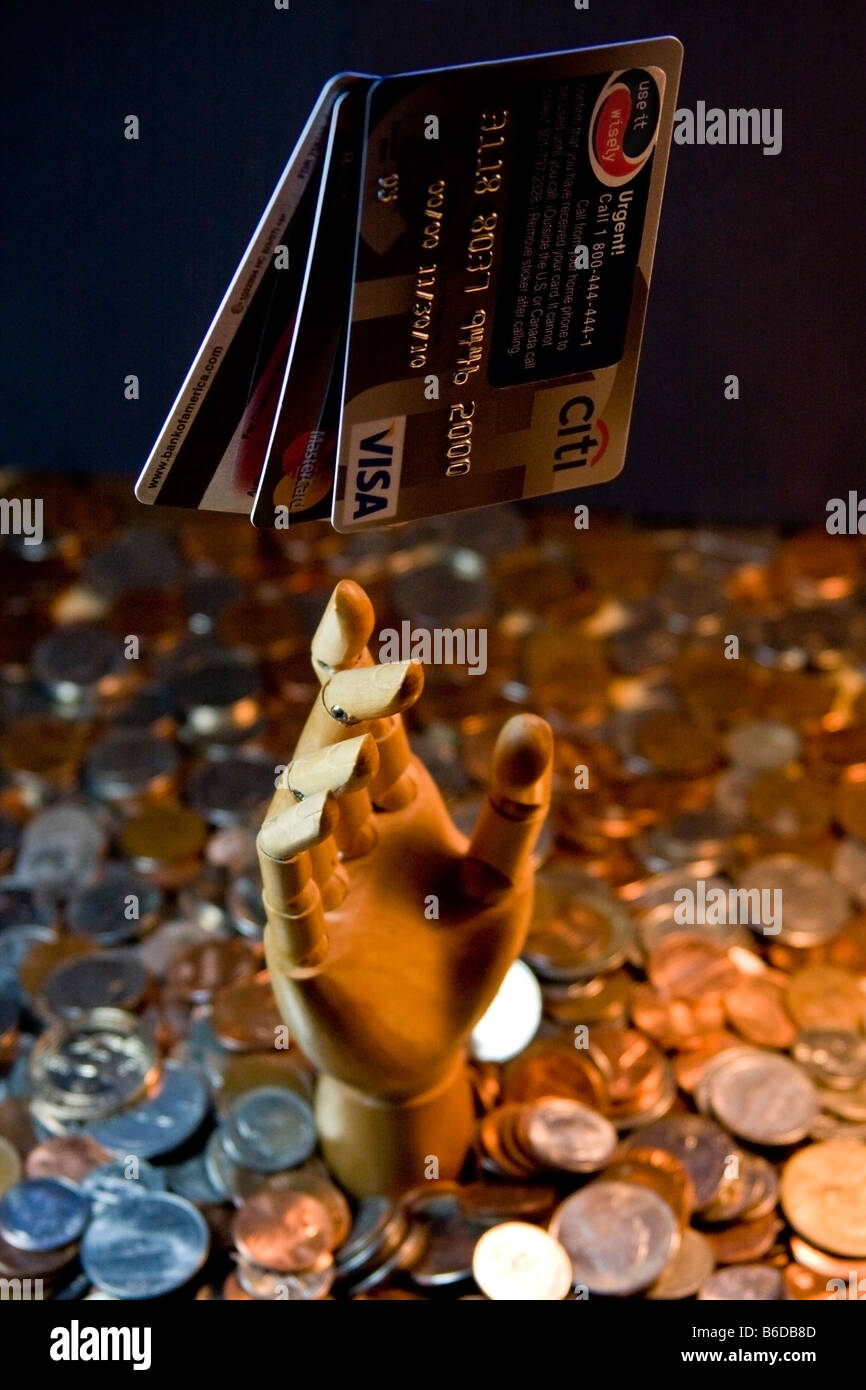 Kredit-Karten hängen in der Luft ausgesetzt, während eine hölzerne mechanische Hand ergibt sich aus einem Meer von US-Münzen, Schulden darstellt. Stockfoto