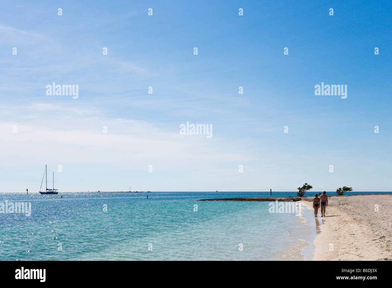 Paare, die am Strand mit einer Yacht in der Ferne, Sombrero Strand, Vaca Key, Marathon, Florida Keys Stockfoto