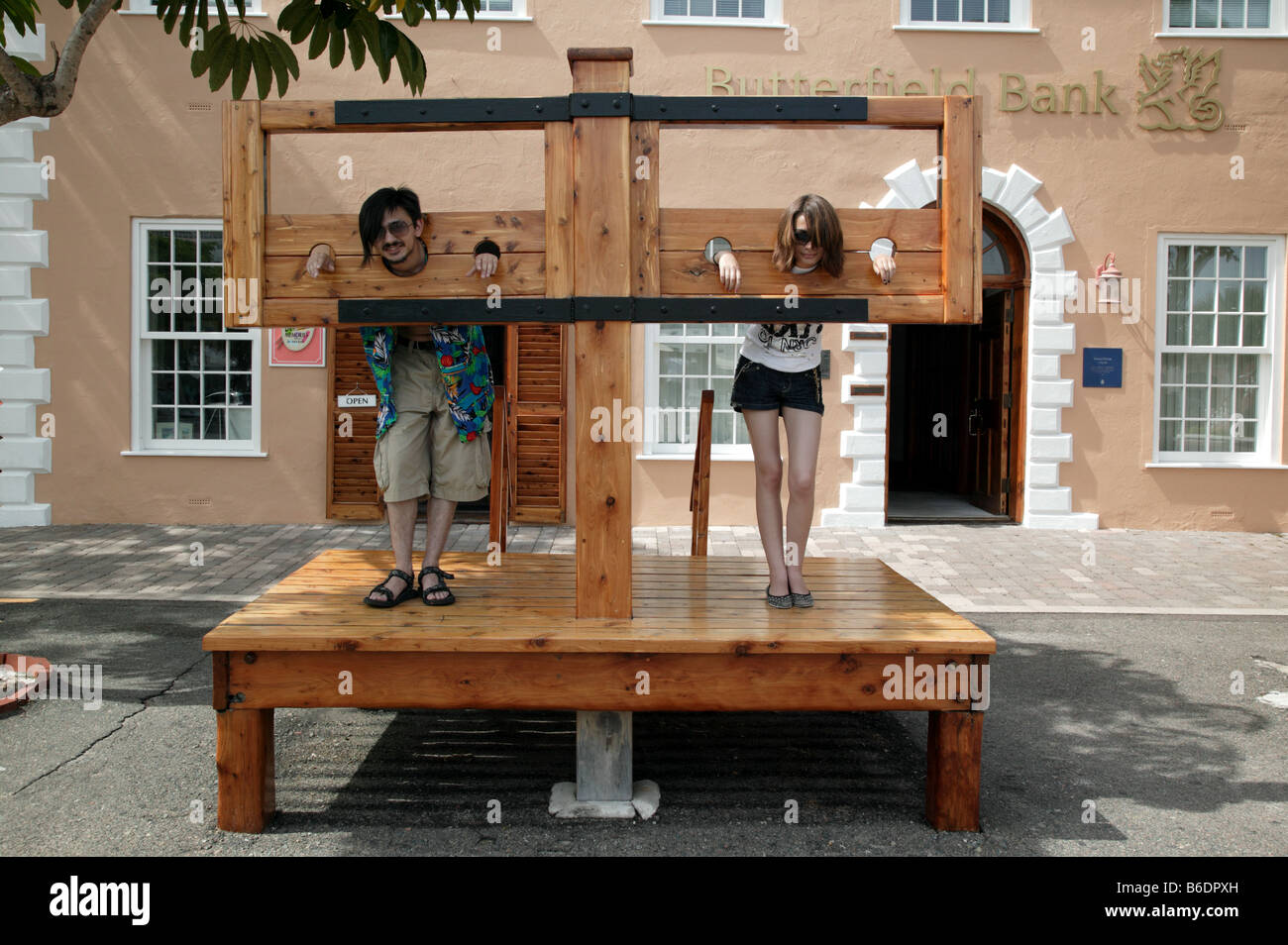 Junger Mann und Mädchen posieren in ein Replikat Pranger in der historischen King Square, St. George, Bermuda Stockfoto