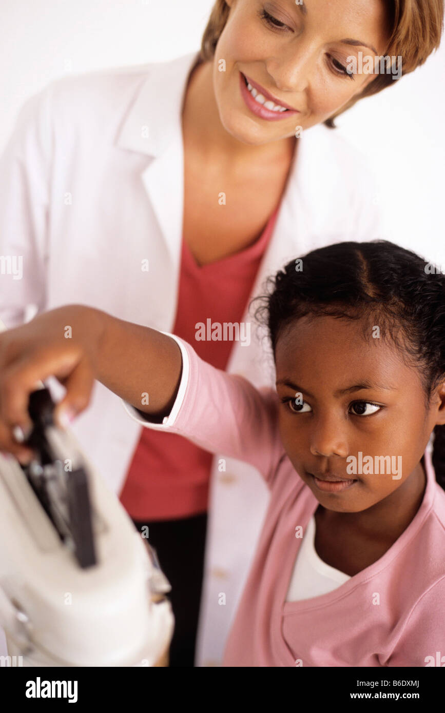 Gewichts-Check-Up. Allgemeinmedizin Arzt beobachten ihre 9 jährige Patientin die Balance auf die Waage. Stockfoto