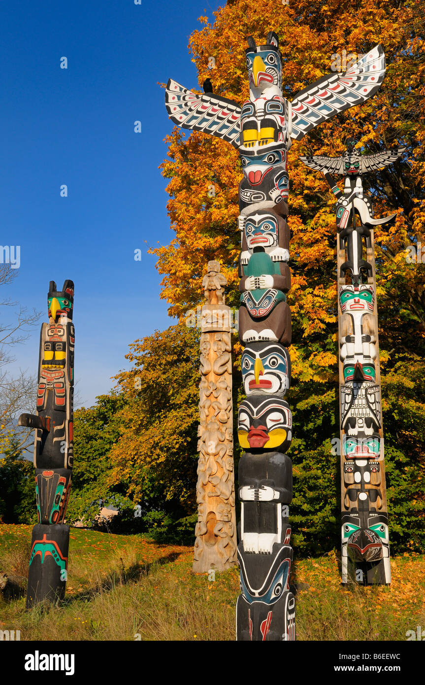 Holzschnitzerei Aborigines Totempfähle im Stanley Park Vancouver mit Raven und ändern Ahorn Blätter im Herbst auf blauen Himmel Stockfoto