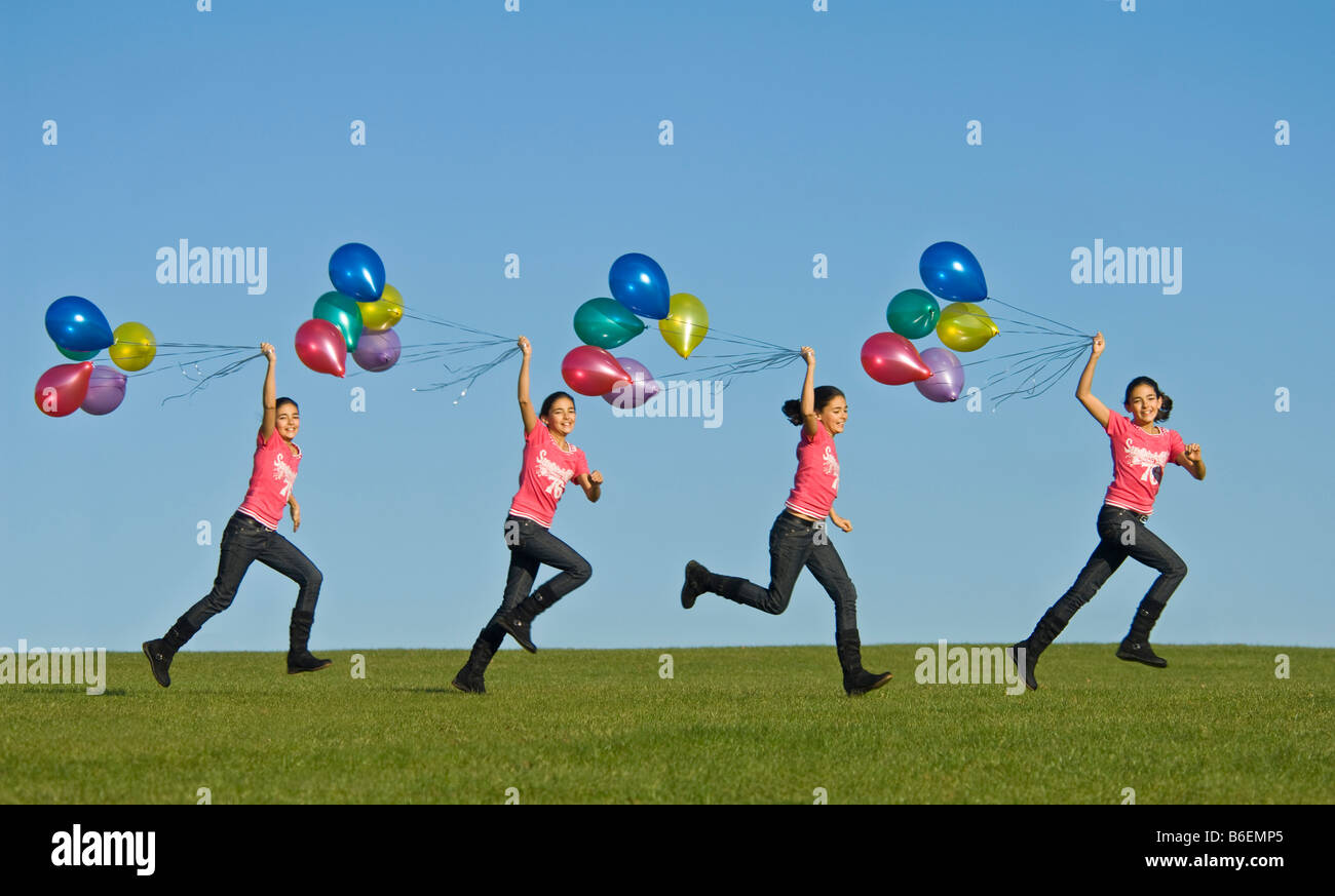 Ein Bild der Sequenz ein junges Mädchen (11) laufen glücklich über grünen Rasen mit einem Bündel von Ballons hinter und blauer Himmel. Stockfoto