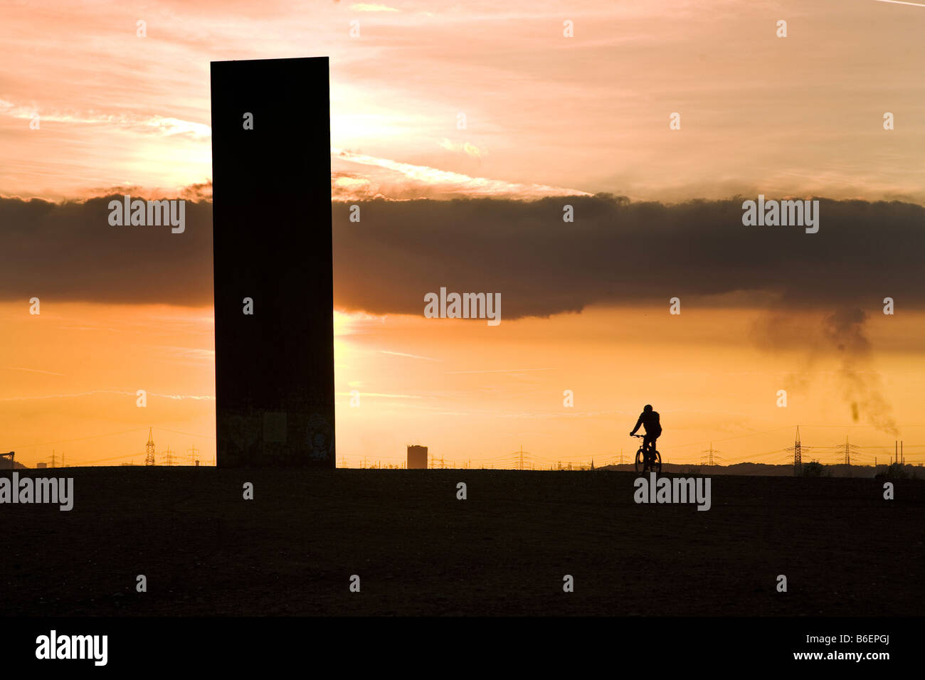 Radfahrer und Werk bei Gegenlicht auf Schurenbachhalde, eine alte Bergbau Müllkippe, Essen, Ruhrgebiet, Nordrhein-Westfalen, Deutschland Stockfoto