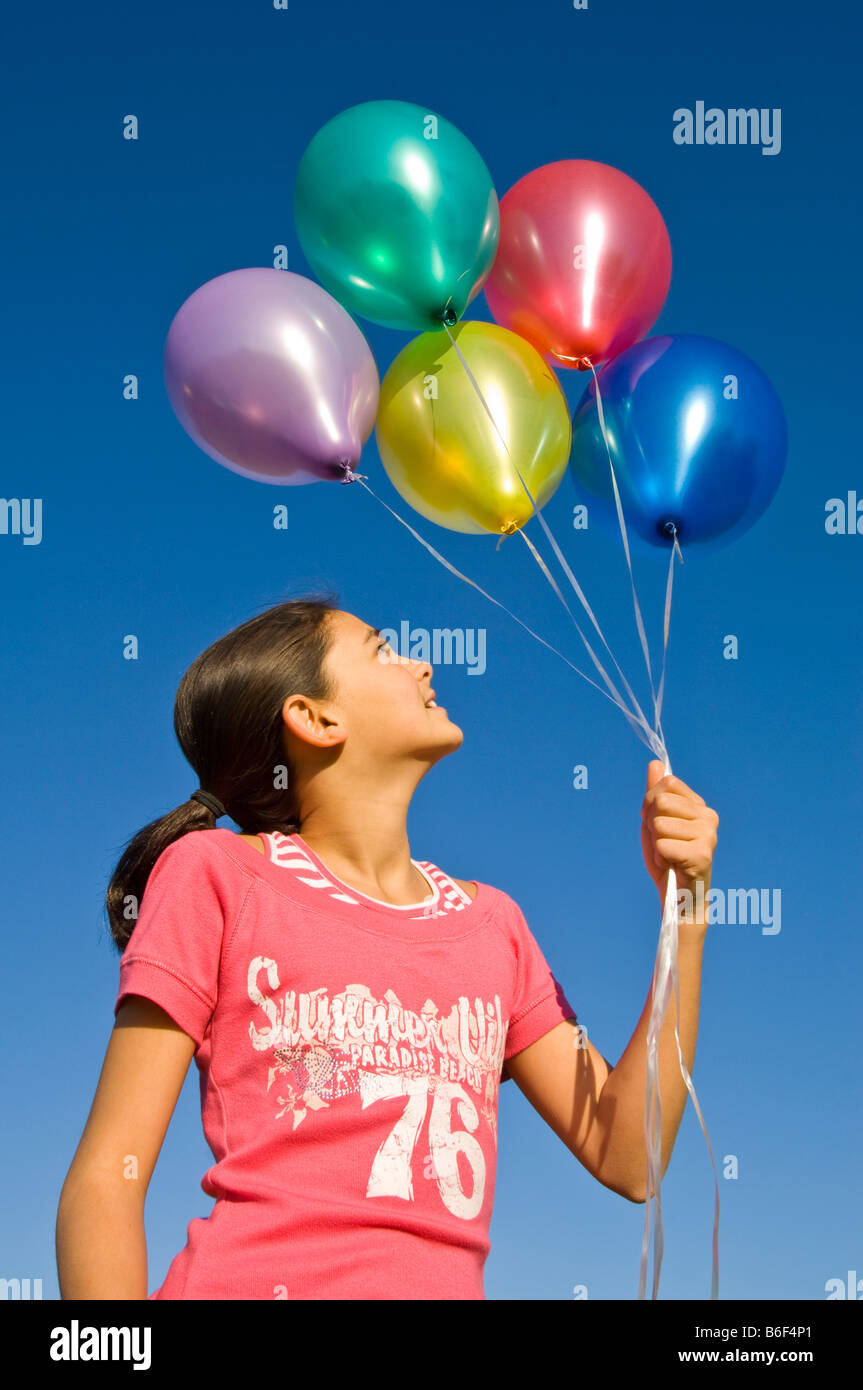 Nahaufnahme eines jungen Mädchens (11) lächelnd mit einer Reihe von bunten gefüllte Heliumballons vor blauem Himmel. Stockfoto