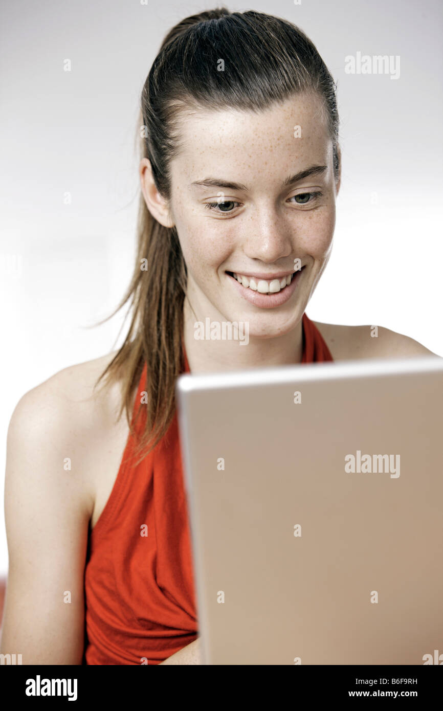 Teenager-Mädchen, Frau, 17 Jahre alt, arbeitet an einem Laptop, trägt ein rotes Kleid Stockfoto