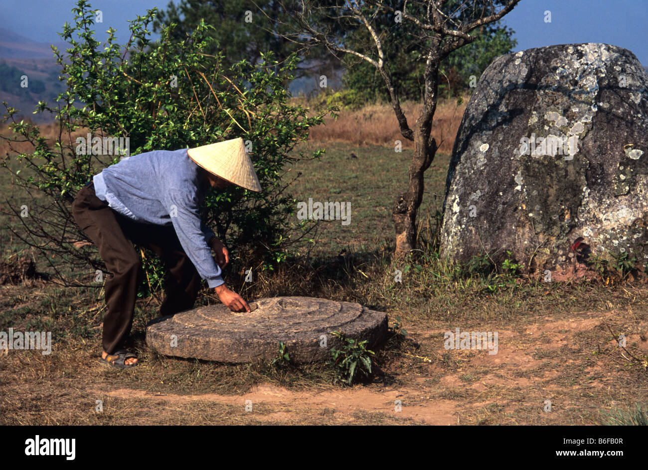 Ein laotischer Dorfbewohner mit dem geschnitzten Deckel von einem riesigen Stein jar auf Plain of Jars (Seite 2), Phonsavan, Xieng Khuang, Laos Stockfoto