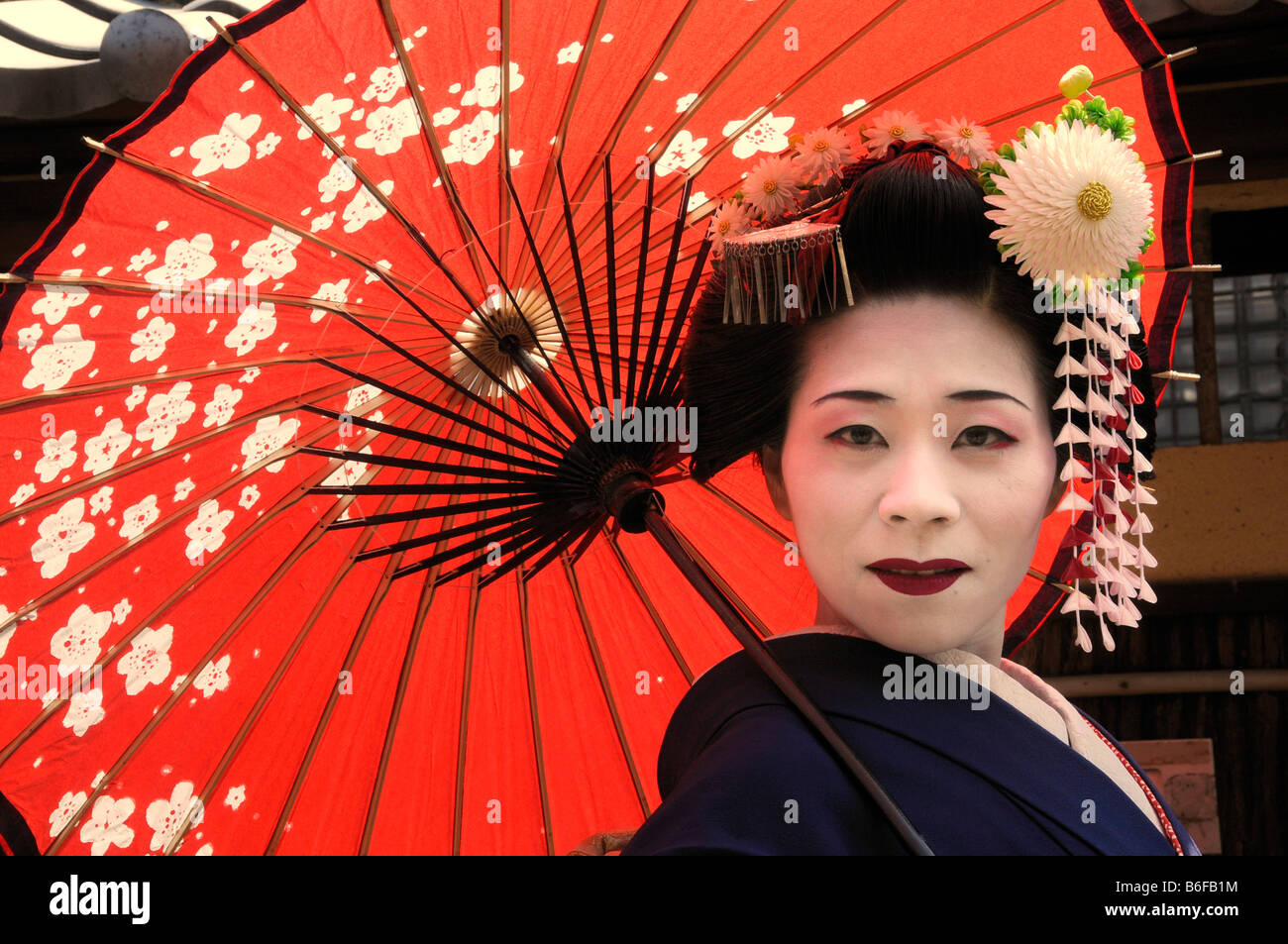 Maiko, Trainee Geisha, die mit einem roten Sonnenschirm oder Regenschirm, Kyoto, Japan, Asien Stockfoto