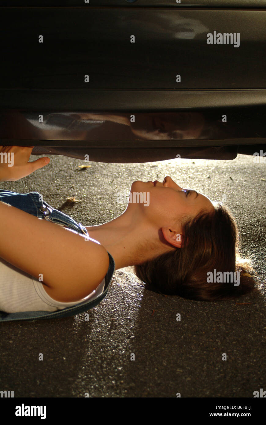 Junge Frau in Arbeitskleidung ist unter ihrem Auto liegen, während es zu reparieren Stockfoto