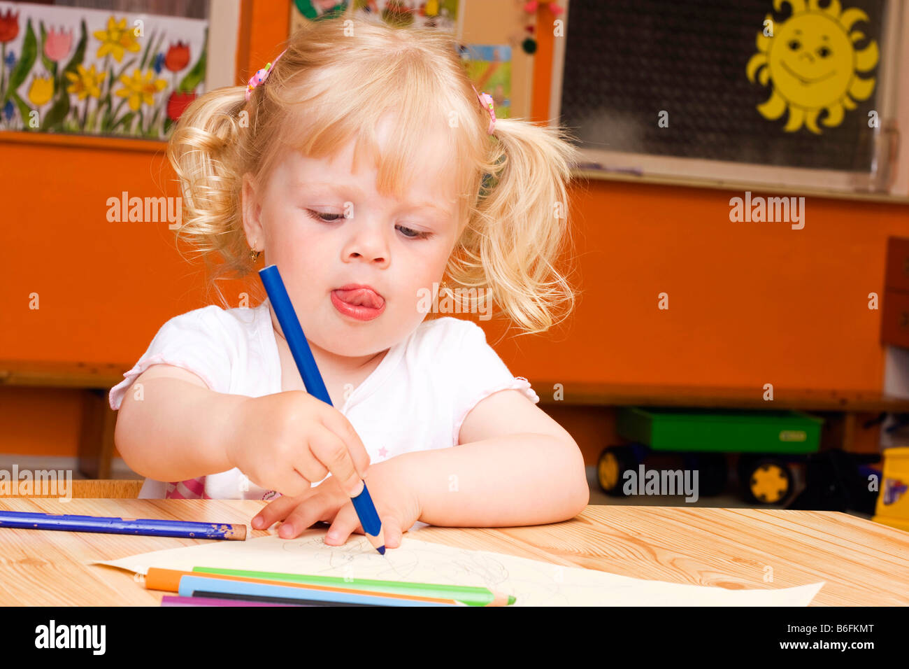 Blondes Mädchen, 3 Jahre, mit Buntstiften am Tisch sitzen Stockfoto