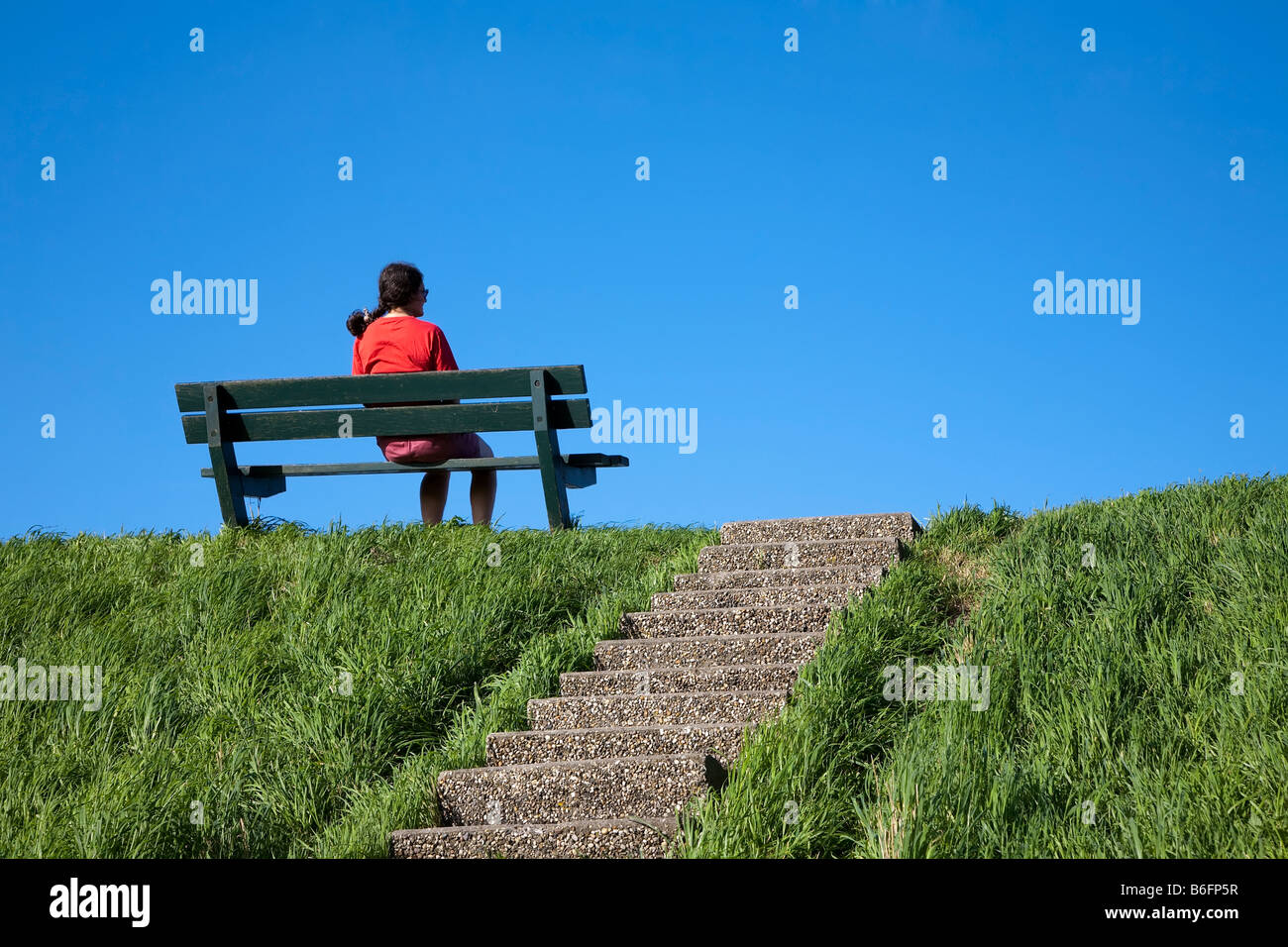 Frau sitzt in Bank am Deich Niederlande Stockfoto