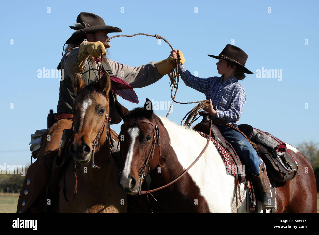 Ein Cowboy zu Pferd zeigt seinen Sohn wie ein Seil um Rinder Abseilen Lasso fangen zu werfen Stockfoto