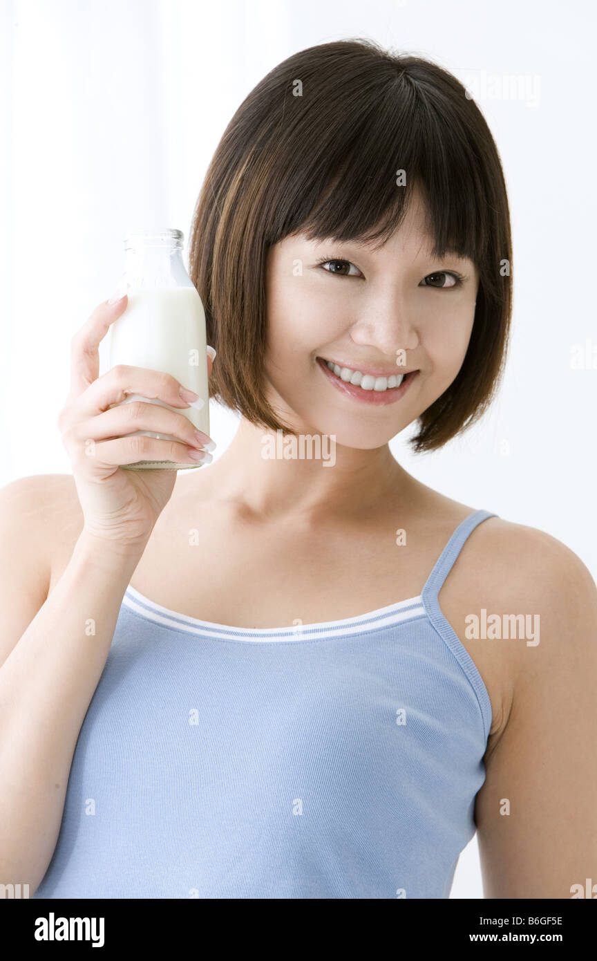 Junge Frau hält eine Flasche Milch neben Gesicht lächelnd Stockfoto