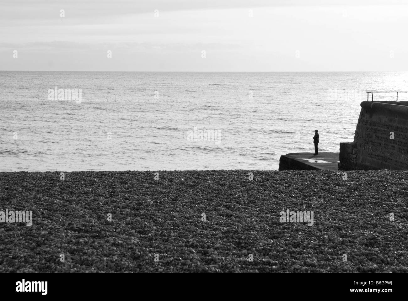 Ein Bild von Brighton Strand mit Kieselsteinen Meer und Himmel. Auf der rechten Seite steht eine Silhouette einer Person am Ende der Mole. Stockfoto