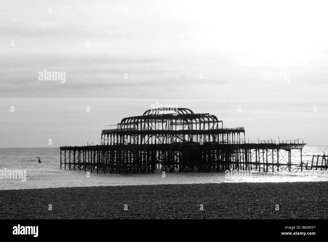 Ein schwarz / weiß Bild der ausgebrannten Überreste Brightons West Pier an einem ruhigen Tag entnommen aus Brighton Beach Stockfoto