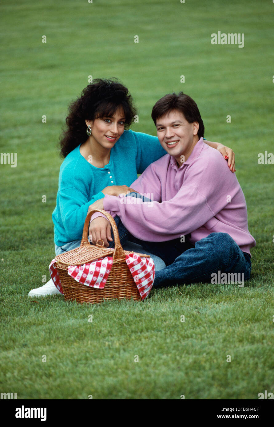 Portrait eines jungen, lächelnd hispanische Ehepaar, das für ein Picknick in einem Park mit dem Rasen im Hintergrund gegangen. Stockfoto