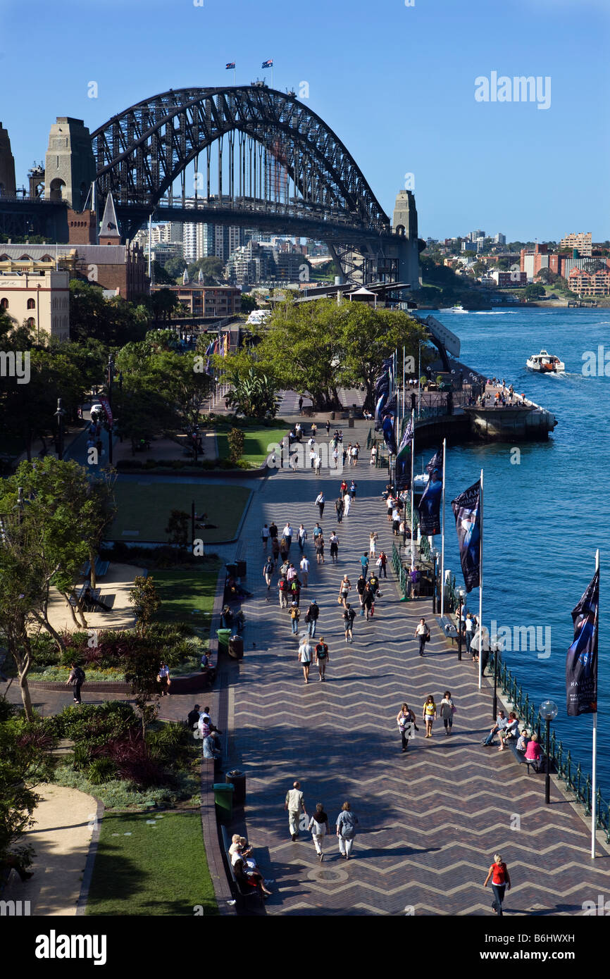 Die Menschen gehen entlang des Hafens von Sydney in The Rocks, mit der Sydney Harbour Bridge im Hintergrund, Sydney, New South Wales Stockfoto