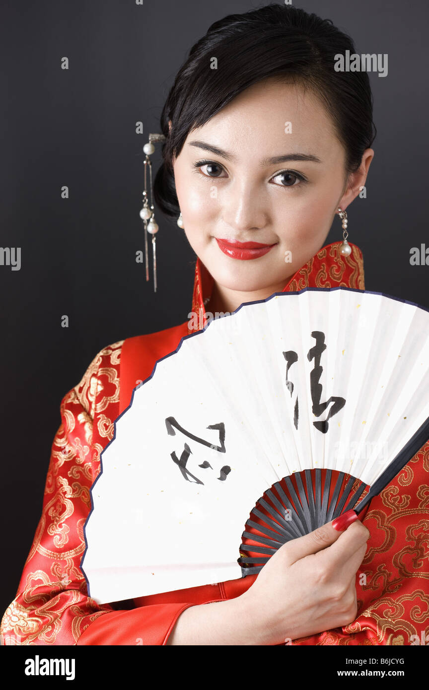 Junge Frau, gekleidet in einen roten traditionelle chinesische Qipao hält ein fan Stockfoto