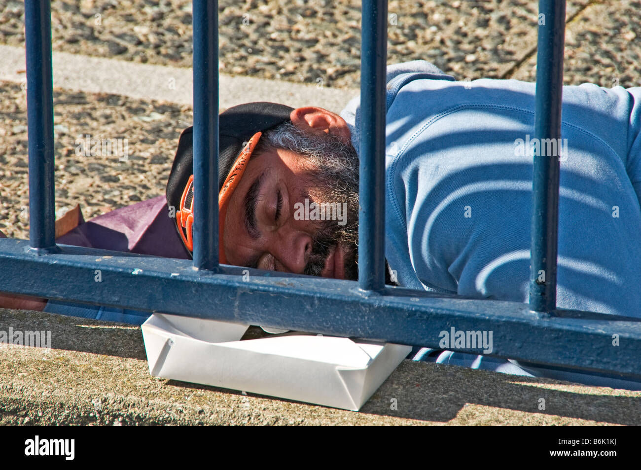 Obdachloser schlafen im Park in der Nähe von Zaun Stockfoto