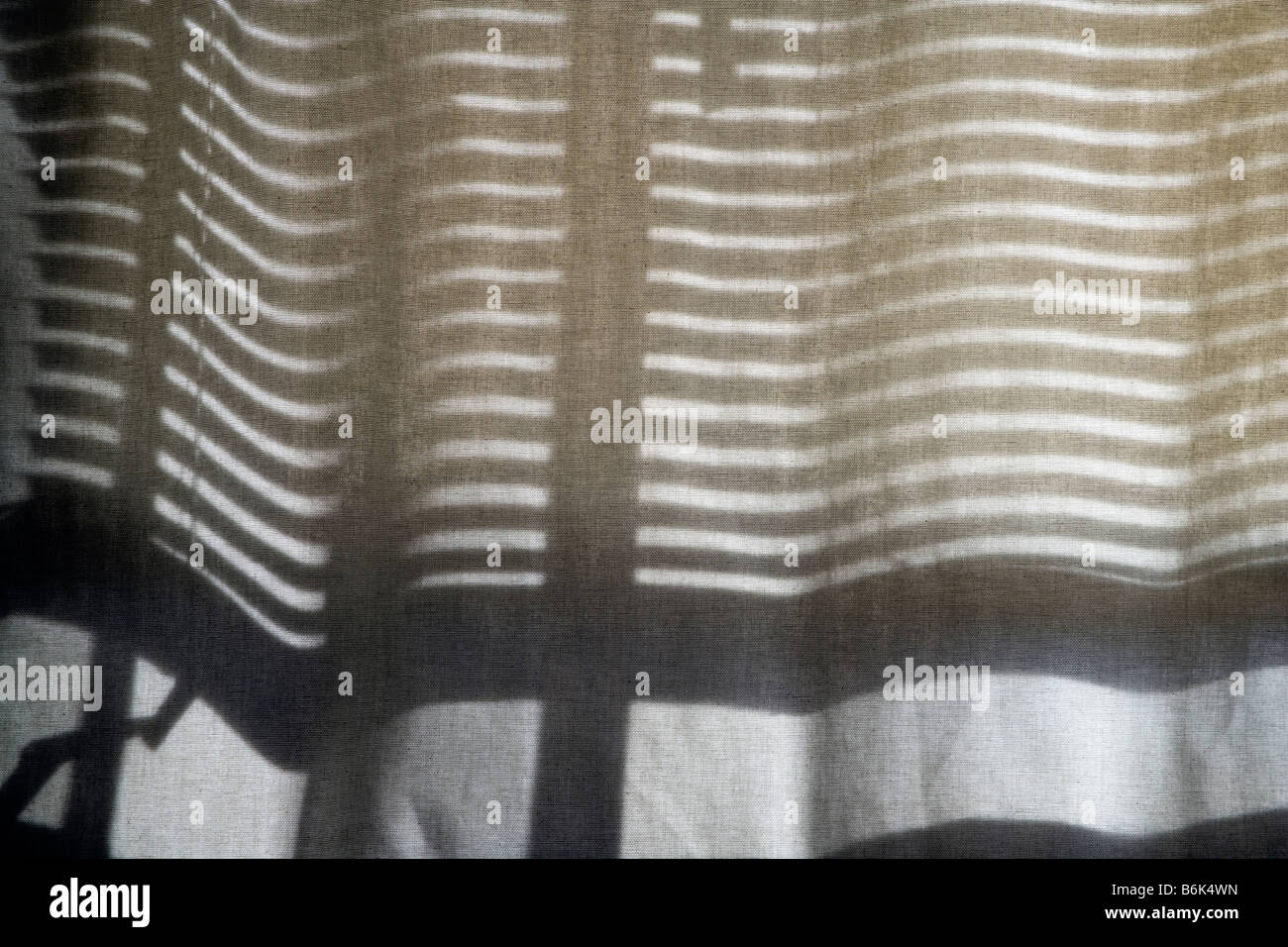 Horizontal-Jalousien werfen eine Muster von Schatten auf einem durchsichtigen Vorhang. Stockfoto