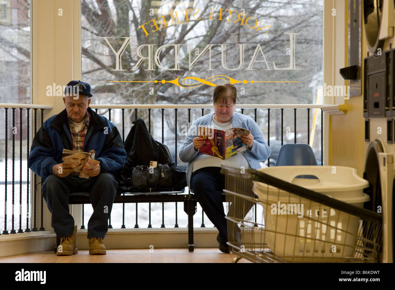 Ältere Paare zusammen sitzen und lesen, wie Sie für Ihre Wäsche bei Waschsalon warten, Münzwaschmaschine. Stockfoto