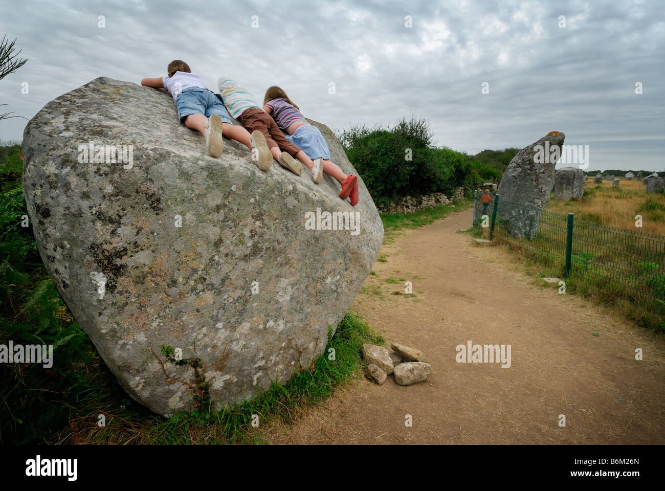 Carnac Bretagne Frankreich drei junge Mädchen, die Verlegung auf einen riesigen Stein am megalithischen Ort der Menec Stockfoto