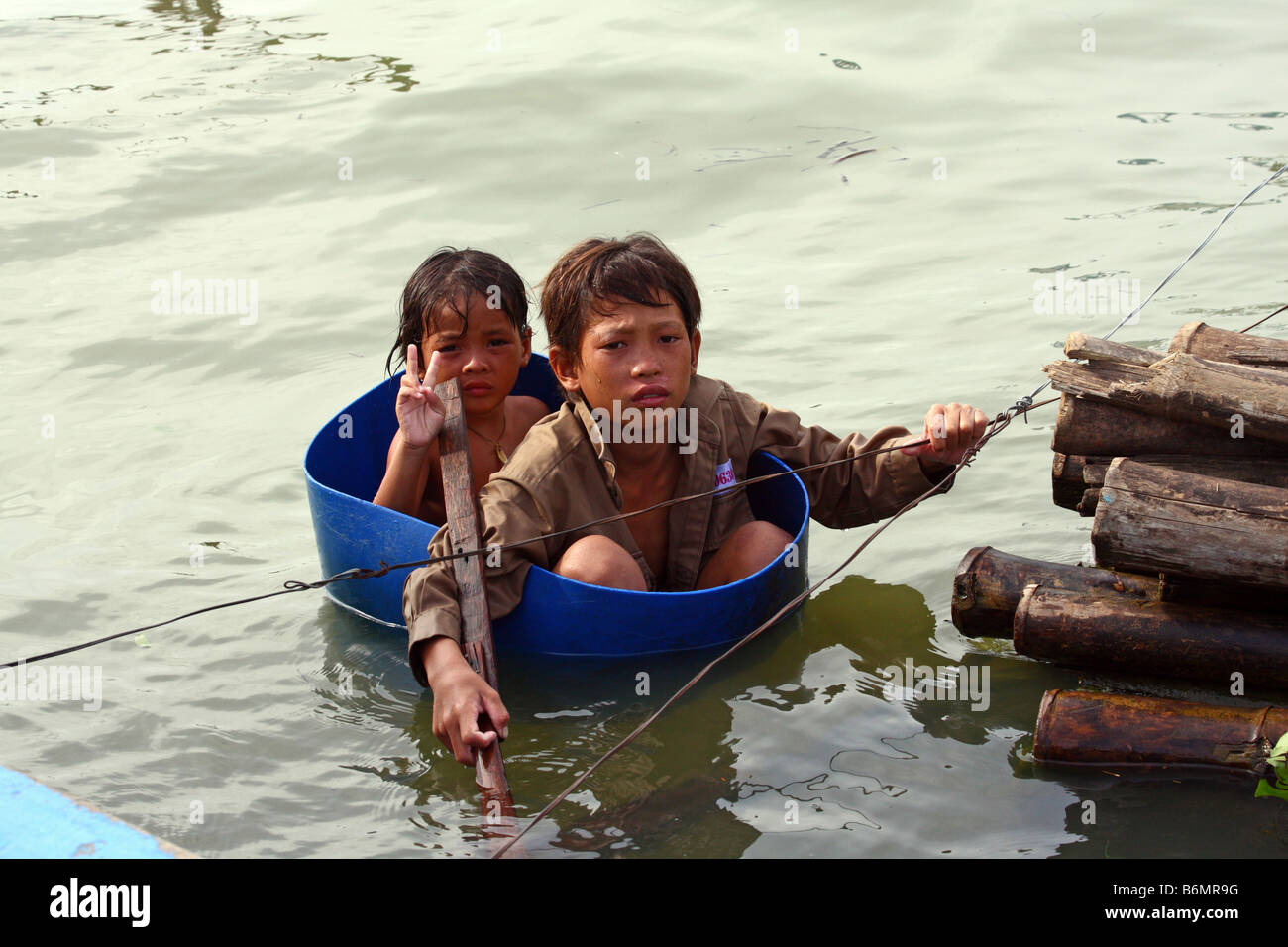 Junge Mädchen tun ein Siegeszeichen V und junge mit einer Schüssel als Boot in schwimmenden Dorf Chong Kneas, Tonlè-SAP-See, Kambodscha Stockfoto