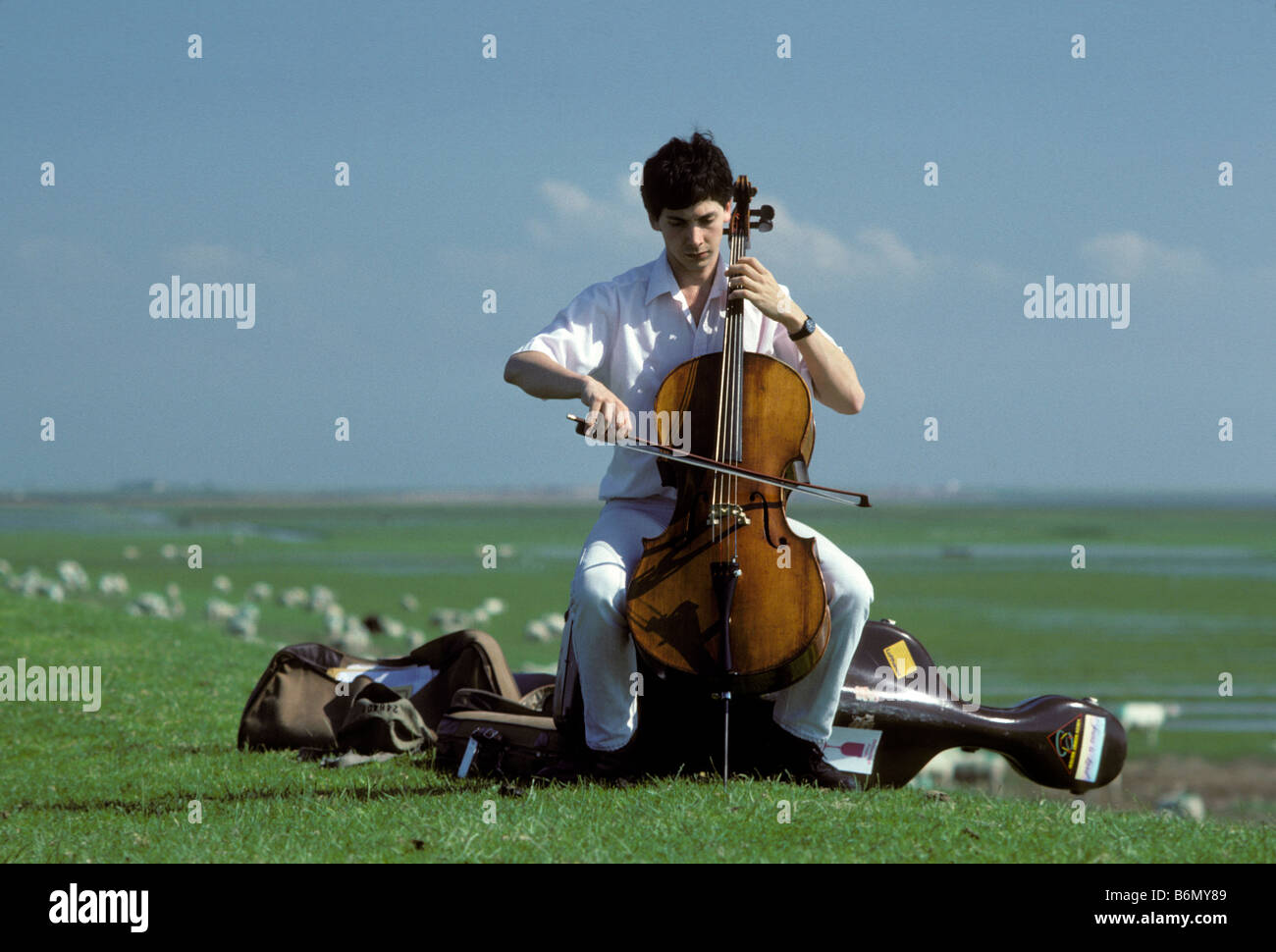 Junger Mann spielt Cello auf dem Deich an der Nordsee in Schleswig-Holstein während der Schleswig-Holstein-Musik-Festival, SHMF. Stockfoto