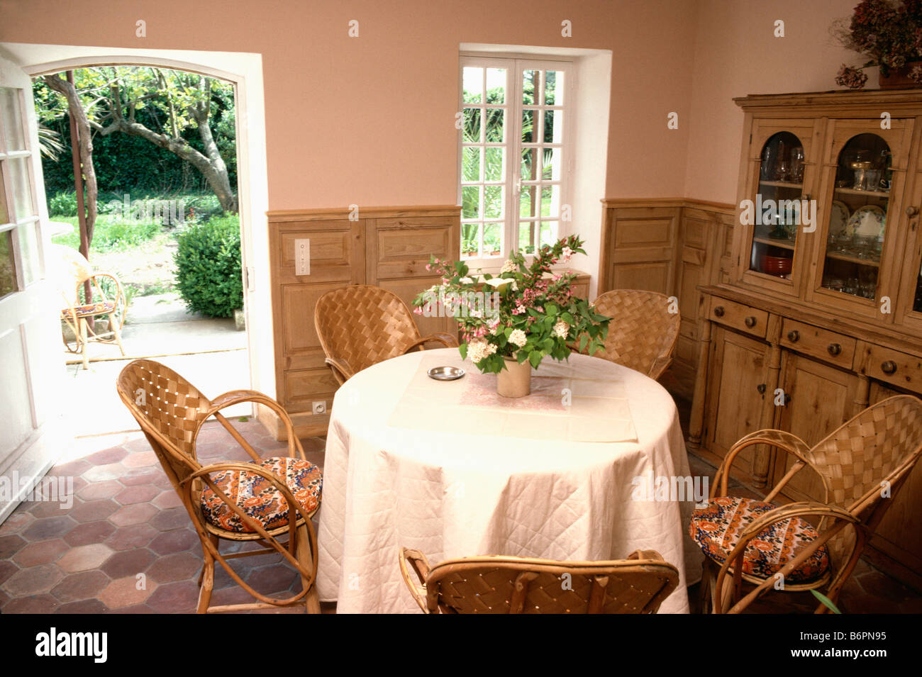 Weiß gesteppt Tuch am runden Tisch mit Rattanstühlen in Pfirsich  französische Land-Ess-Zimmer mit Tür zum Garten Stockfotografie - Alamy