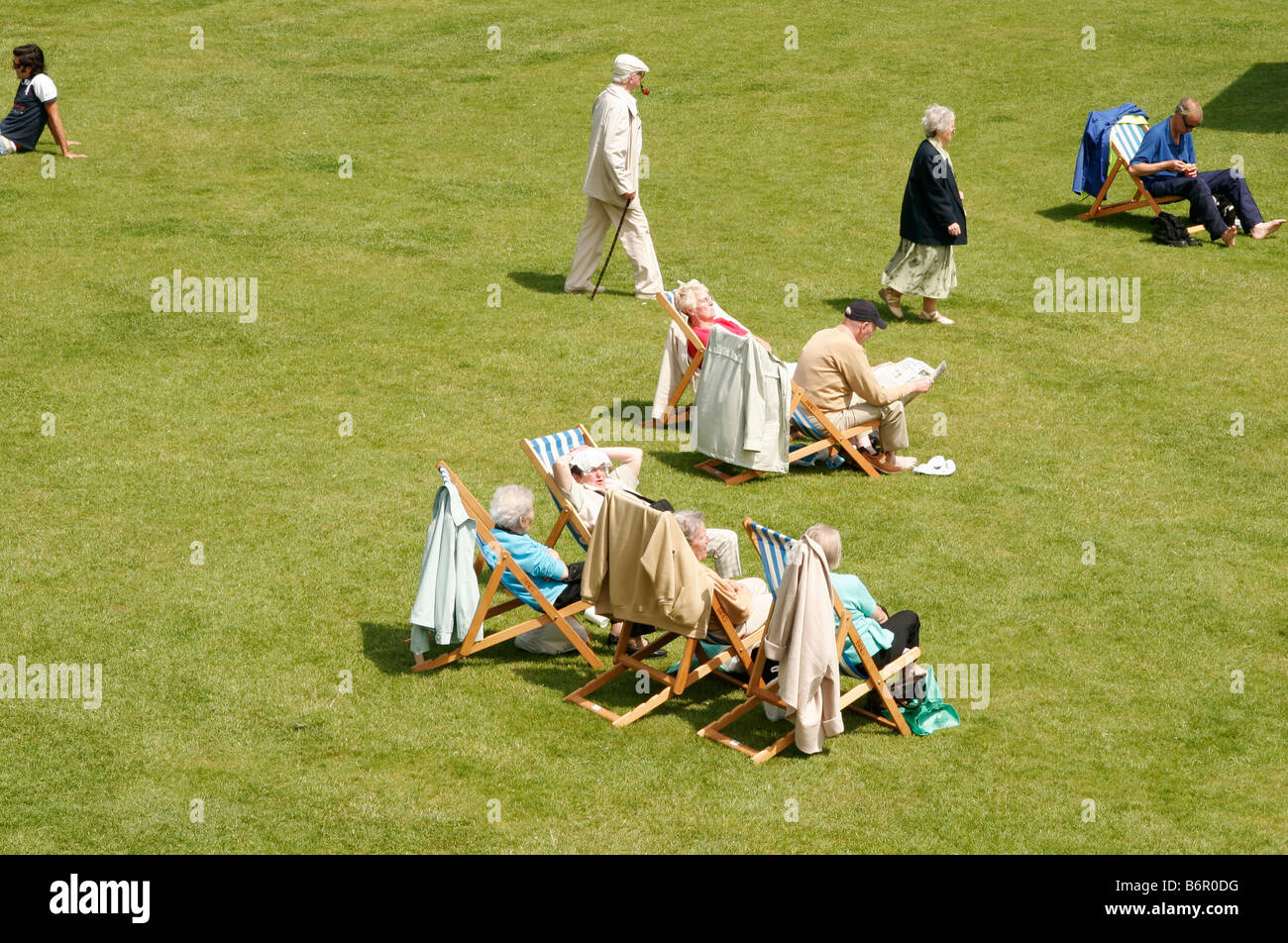 Menschen sitzen auf Liegestühlen und gehen auf dem Rasen im Park Garten an einem sonnigen Sonntag Nachmittag Stockfoto