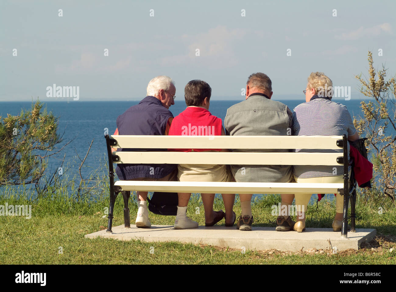 4 ältere Menschen zwei Paare sitzen auf einer Bank am Meer mit einem Chat Senioren auf Urlaub am Meer Stockfoto