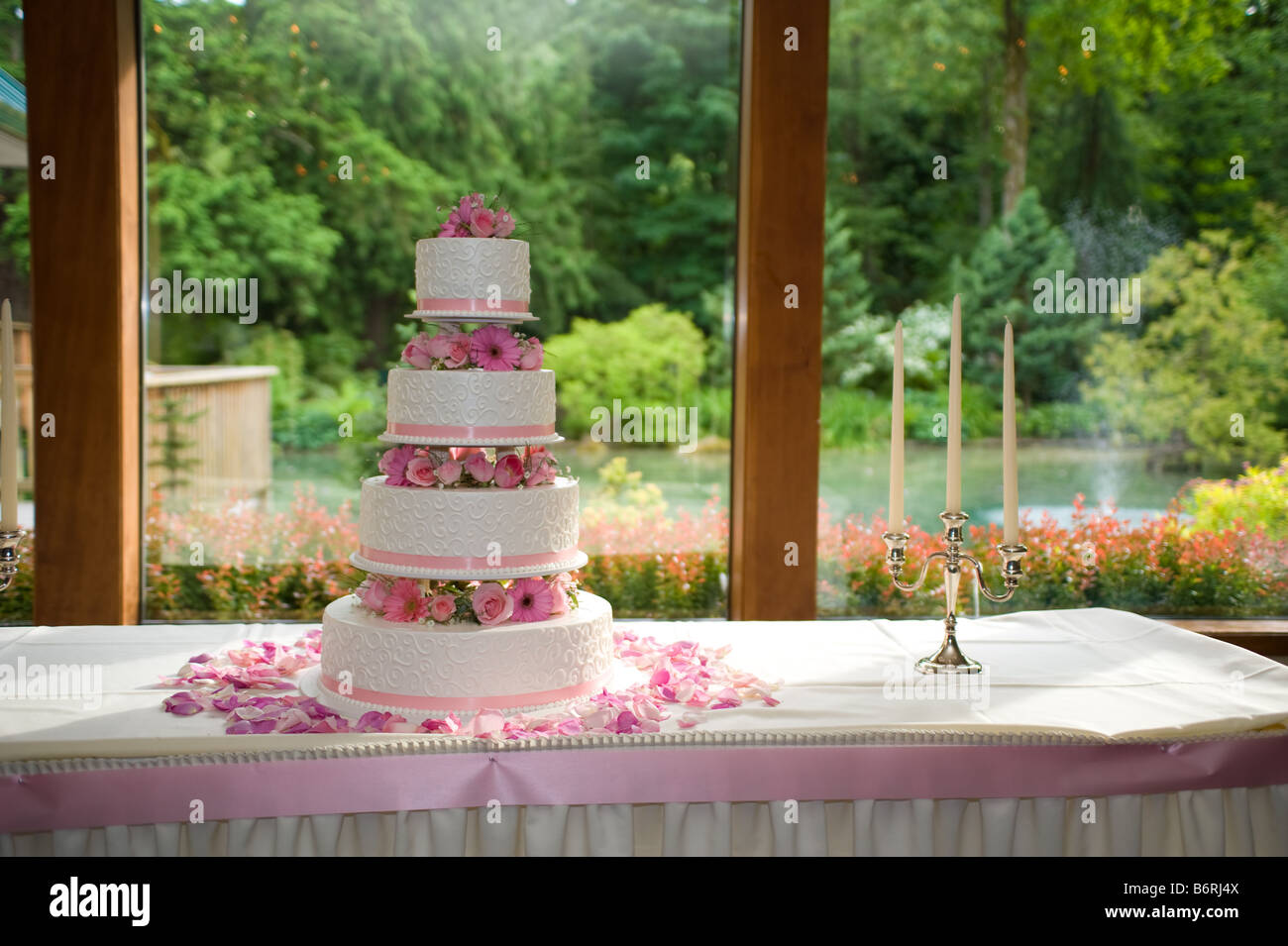 Rosenblätter verstreut eine Multi Tier Hochzeitstorte durch ein Fenster mit Aussicht Stockfoto