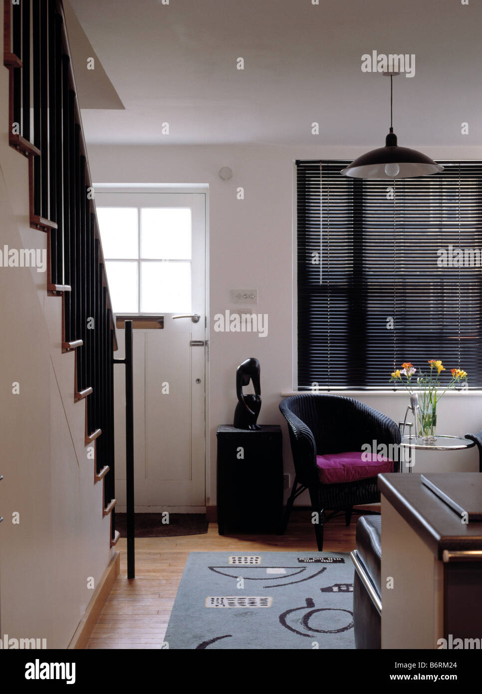 Schwarz Lattenrost blind und schwarz Sessel in kleinen Küche mit gemusterten Teppich neben Treppe Stockfoto