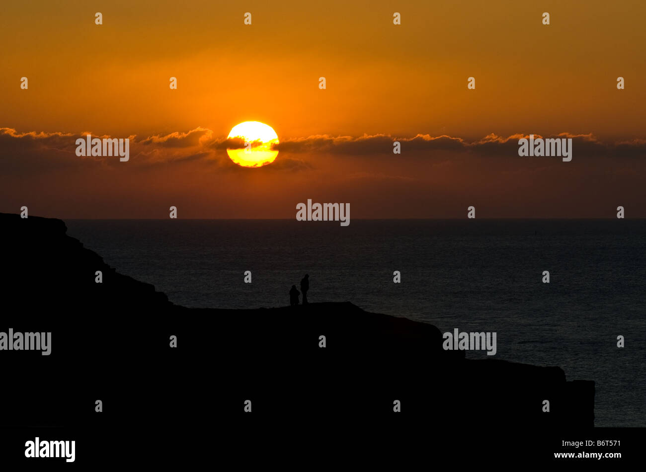 Zwei Personen suchen in einen spektakulären Sonnenuntergang am Rhossilli an der Gower Küste in Wales. Stockfoto