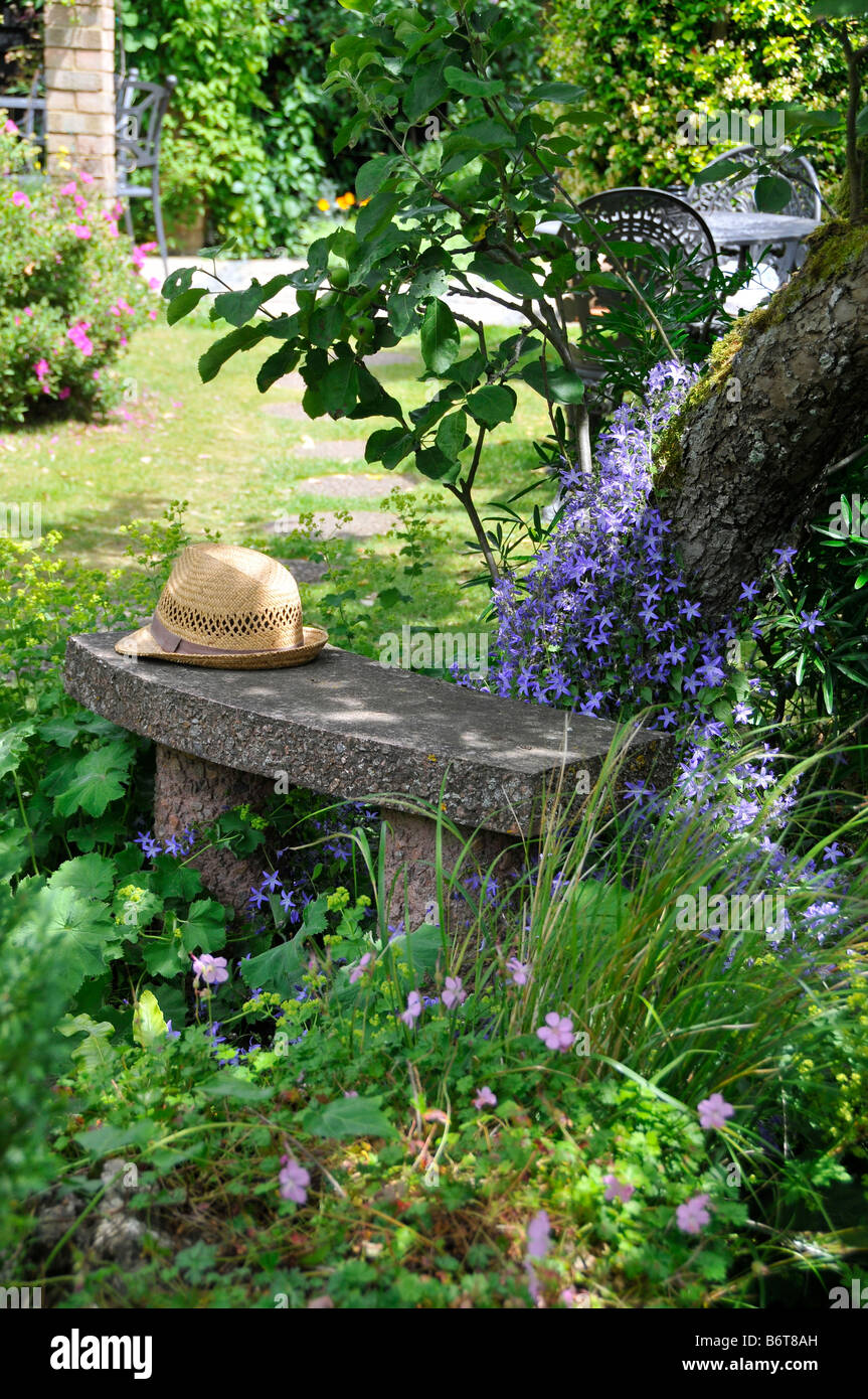 Traditionelle englische Garten Szene mit Strohhut auf Bank unter Baum, umgeben von Blumen Stockfoto