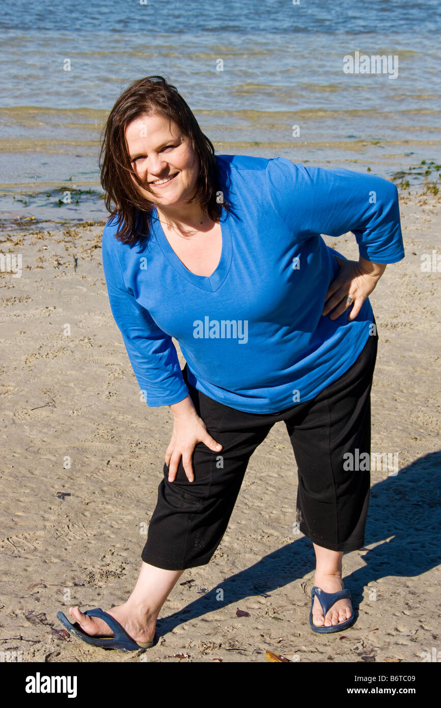 Plus Größe Frau am Strand erstreckt sich im Rahmen des Fitness-Programm Stockfoto